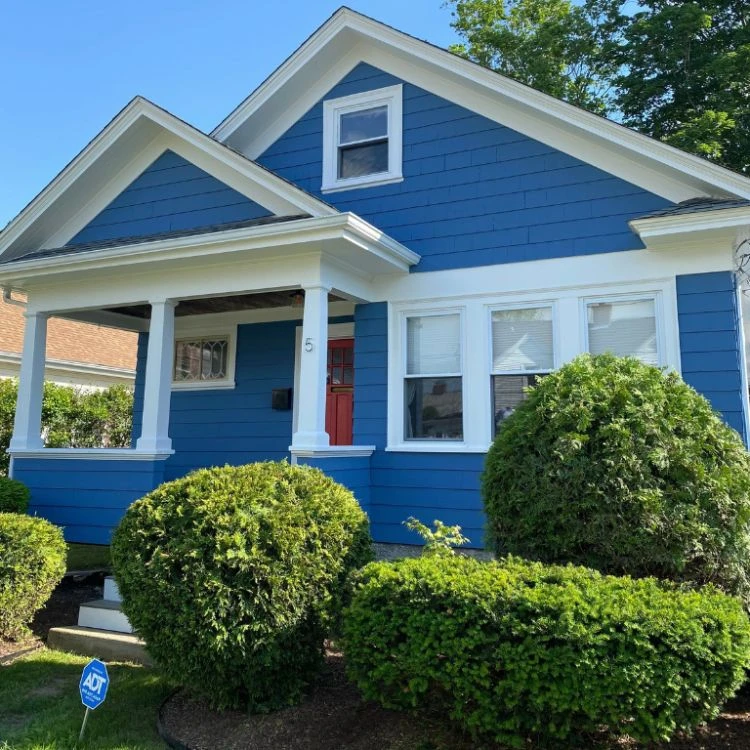 ArchRI2 A blue house with white trim and bushes, expertly painted by Arch Painting in Rhode Island.